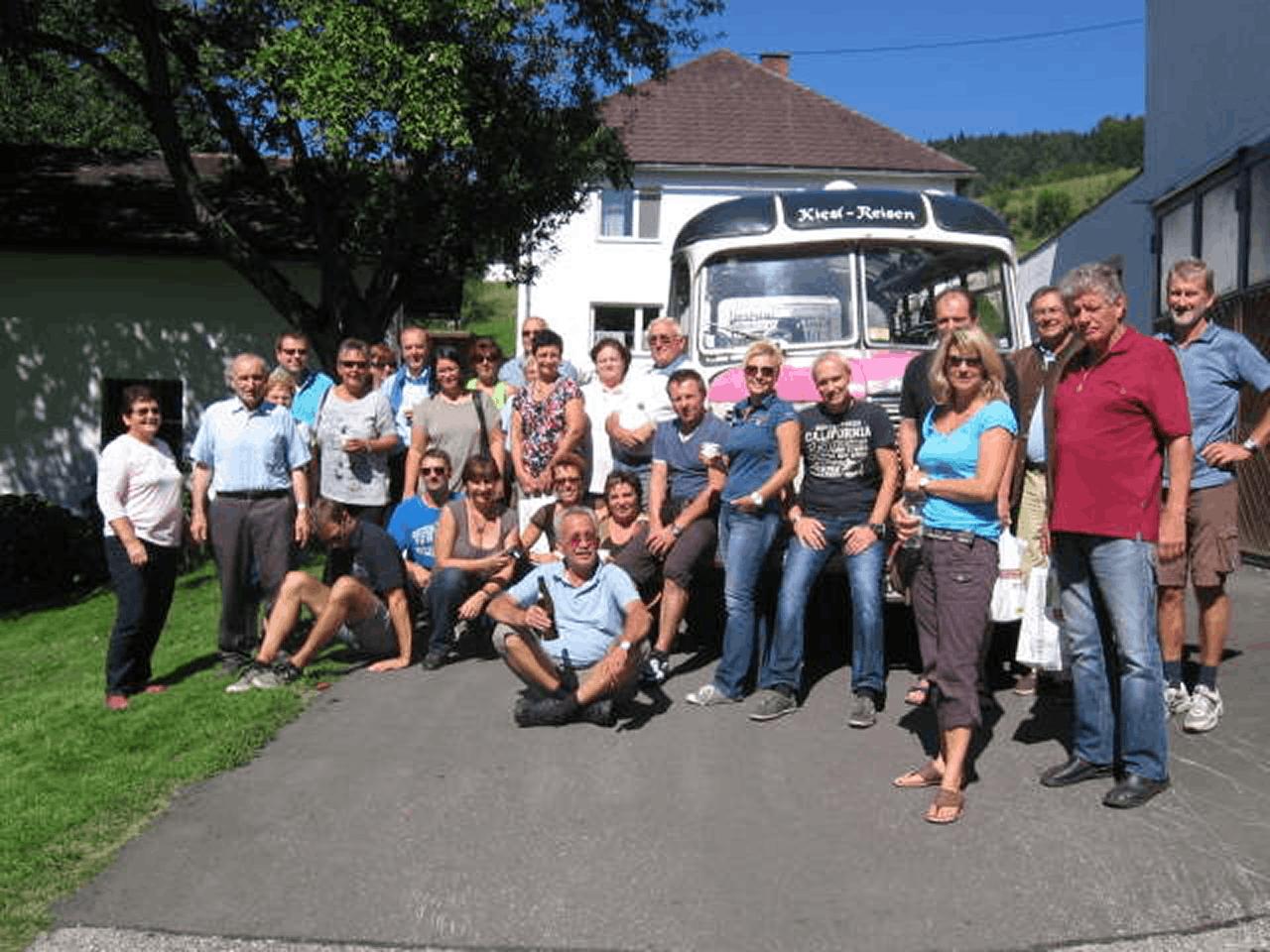 Große Besuchergruppe posiert vor einem Reisebus des Unternehmens „Kiesl-Reisen" bei einem Ausflug zur Erlebnis-Imkerei Hüttner.
